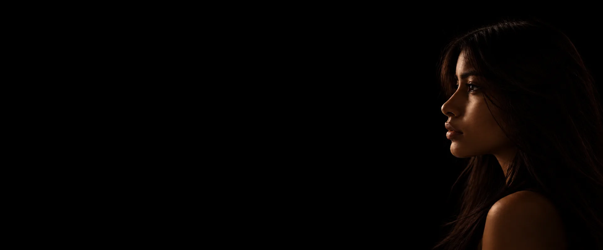 A woman’s profile lit low against a black ground, eyes turned to the light